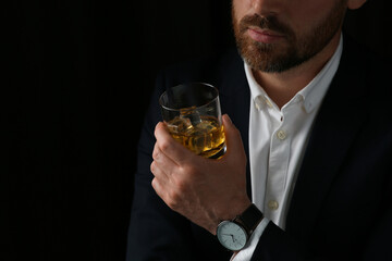 Man holding glass of whiskey with ice cubes on black background, closeup