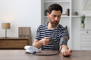 Man measuring blood pressure at wooden table in room
