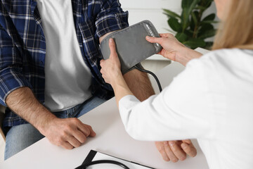 Doctor measuring blood pressure of man at table indoors, closeup