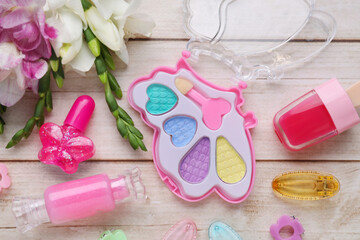 Decorative cosmetics for kids. Eye shadow palette, lipsticks, accessories and flowers on white...