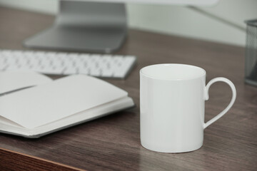 White ceramic mug on wooden table at workplace. Mockup for design