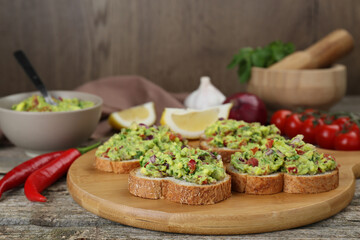 Slices of bread with tasty guacamole and ingredients on wooden table, closeup