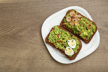 Slices of bread with tasty guacamole, eggs and shrimp on wooden table, top view. Space for text