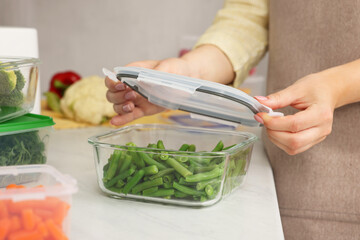 Woman sealing glass container with lid at white marble table in kitchen, closeup. Food storage