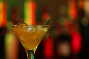 Martini glass with cocktail, ice cubes and rosemary in bar, closeup. Space for text