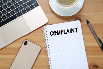 Notebook with word Complaint, laptop, phone and cup of coffee on wooden table, flat lay