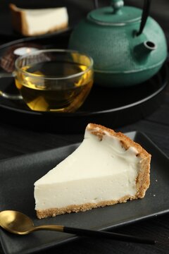 Piece of tasty vegan tofu cheesecake and spoon on black wooden table, space for text