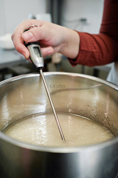 Close-up view of unrecognizable female cook measuring temperature of melting sugar in saucepan with modern kitchen thermometer 