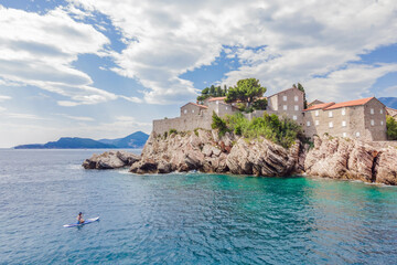 Fototapeta na wymiar Young women Having Fun Stand Up Paddling in blue water sea near st stefan island in Montenegro. SUP