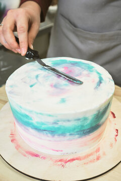 Close-up view of unrecognizable pastry chef smoothing beautiful frosted cake with spatula in confectionery kitchen 