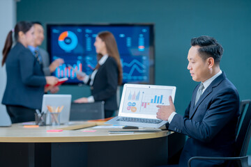 Smiling middle-aged executive asian businessman sitting at a worktable a modern office, typing on computer keyboard, and talk to work, sending emails to his business partners, working on marketing.