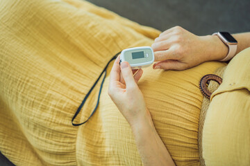 Pregnant woman with pulse oximeter on finger. Doctor measuring oxygen saturation level while visiting expectant mother with coronavirus disease at home, cropped. Pregnancy and covid-19 concept