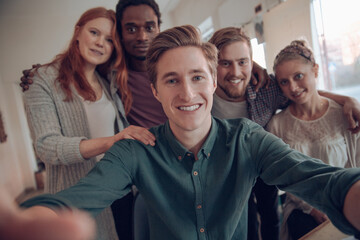 Young and diverse group of coworkers taking a selfie with a smart phone in the startup company office
