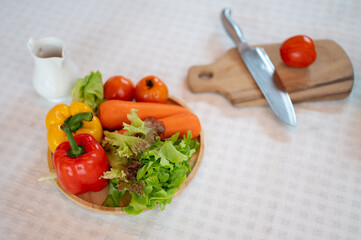 A plate of fresh vegetables, a knife, and a wooden chopping board on a dining table.