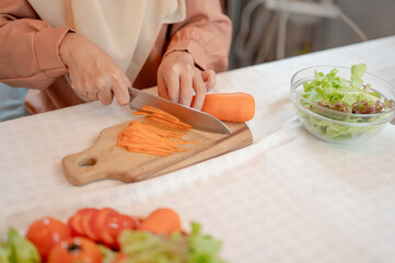 Close-up image of a Muslim woman is slicing carrot with knife on a chopping board