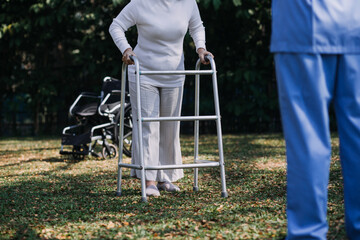 Asian young woman nurse at nursing home take care disabled senior man. Caregiver doctor serve physical therapy for older elderly patient to exercise and practice walking on walker or cane at backyard.