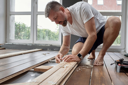 Concentrated man planing wooden board at home