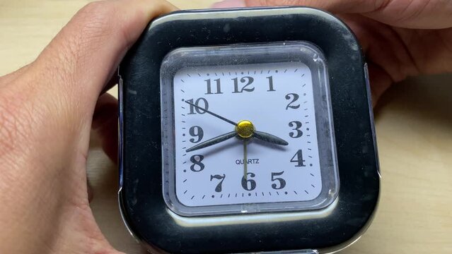 Hands setting up alarm clock tick pointer and rewind table clock close up view. Time and reminder concept