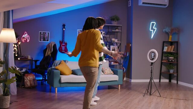 Two Gen Z Asian friends K-pop dancers record trending reels for social media. Dance in K-pop style recording video on smartphone ring lamp. Bloggers shoot video trend virtual life vertical video