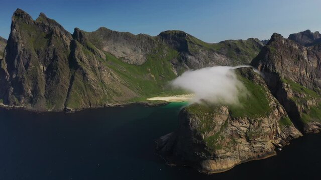 Cinematic wide rotating aerial shot of clouds moving over cliffs at Horseid Beach with turquoise blue water. Northern side of Moskenes&oslash;y, in the western part of Lofoten