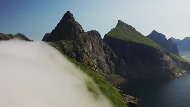 Revealing drone shot of clouds moving over cliffs at Horseid Beach with turquoise blue water.  Northern side of Moskenes&oslash;y, in the western part of Lofoten