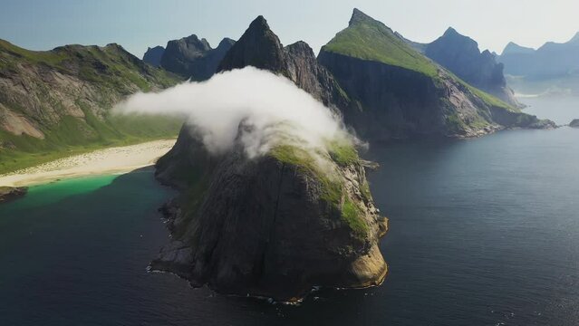 Cinematic wide rotating drone shot of clouds moving over cliffs at Horseid Beach with turquoise blue water. Northern side of Moskenes&oslash;y, in the western part of Lofoten