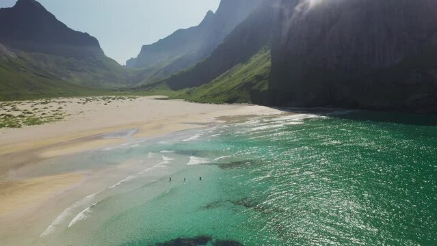 Cinematic wide revealing drone three people swimming at Horseid Beach in turquoise blue water. Northern side of Moskenes&oslash;y, in the western part of Lofoten