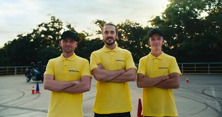 A team of driving instructors in a yellow T-shirt put their hands on their chests and pose. Trio of driving instructors in a driving school