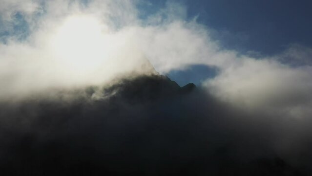 Cinematic drone shot of clouds on top of mountain peaks with the sun casting shadows in the clouds. Northern side of Moskenes&oslash;y, in the western part of Lofoten