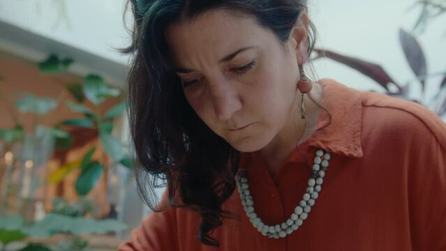 Woman using tweezers to clean plants inside of terrarium in glass jar while taking care of an indoor home garden