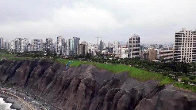 Aerial orbital shot showing a paraglider doing wingovers over the highway while cars are driving below