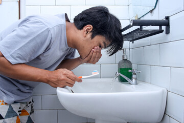 Young Asian man cleaning mouth while toothbrushing in the bathroom - obrazy, fototapety, plakaty