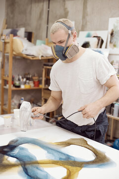Man blowing on canvas with paints making abstraction