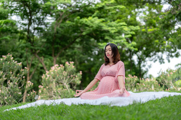 Portrait of asian pregnant woman relaxing by meditating in park