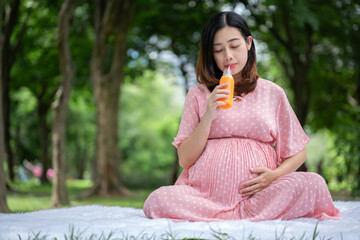 Portrait of Asian pregnant woman relaxing and drinking orange juice in the park