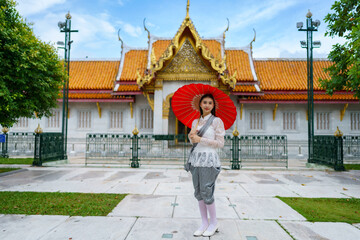 Portrait of beautiful young woman wearing Thai Rattanakosin national costume in a temple built...