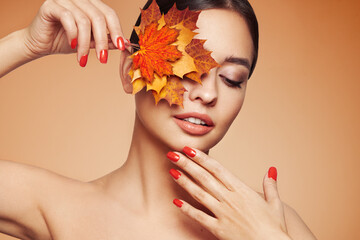 Naklejka na ściany i meble Portrait of beautiful young woman with autumn leafs. Healthy clean fresh skin natural make up beauty eyes and red nails