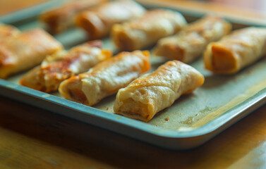 Freshly cooked spring rolls are arranged on a baking sheet. Spring rolls fried in cooking oil. The exterior looks golden and crispy, and the texture is crispy on the outside and tender on the inside. 