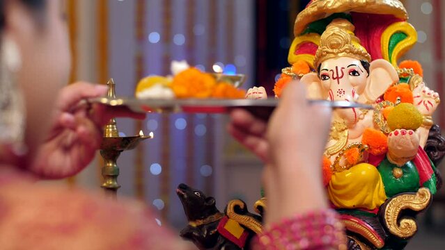 Overhead shot of an Indian female worshipping Lord Ganesha with Puja thali on Ganesh Chaturthi. A female is praying in front of Ganesh Ji with aarti thali in her hand - decorated festival backgroun...