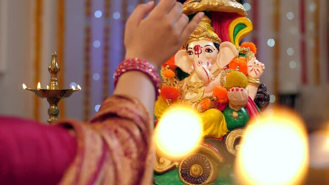 Indian Hindu festival rituals during god prayer  Ganesh chaturthi  colorful decoration   inauguration  starting new business  taking blessings. Female putting a red Tika on the forehead of Lord Gan...