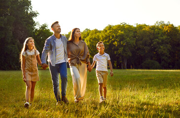 Parents and children take a stroll in nature. Happy mother, father and children holding hands and walking together on a grass lawn in a beautiful green park on a good sunny summer day. Family concept