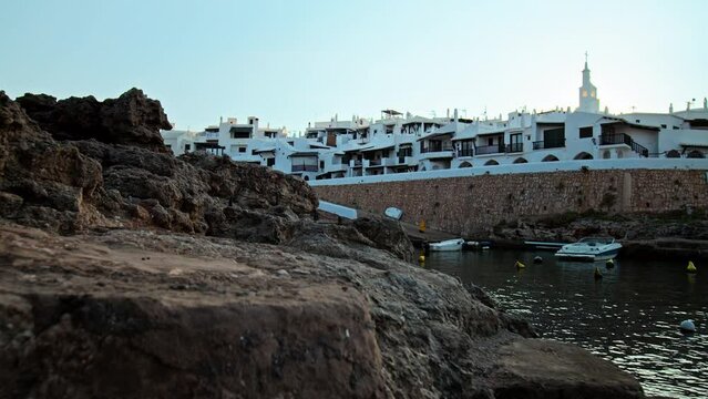 Beautiful rocky seashore with Binibeca Vell in the background in Menorca, Spain. A view of a Spanish resort with hotels and relaxing nature on the Balearic Islands.