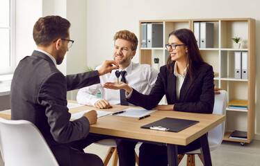 Real estate agent gives house key to happy family couple. Realtor sitting at office desk together with young man and woman and giving them key to their new house or apartment. Buying property concept