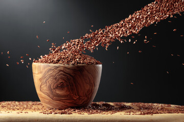 Grains of flaxseed are poured into the wooden bowl.