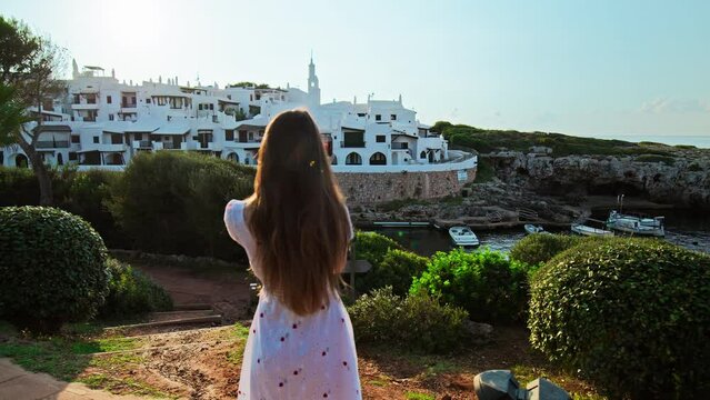 A tourist girl filming with her phone on a gimbal at a Spanish Resort in Menorca. Female explorers taking photographs of whitewashed houses in Binibeca Vell, Balearic Islands