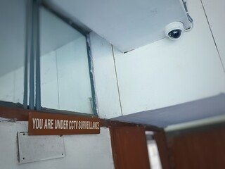 CCTV camera installed above a gate in library along with sign that says you are under cctv...