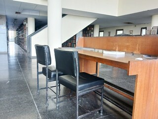 empty black leather chairs with tan colored tables in a library of a university. Interior view of a library with a book on table. 