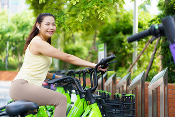 Happy beautiful Asian middle adult woman in sport clothing preparing to ride an electric scooter or...