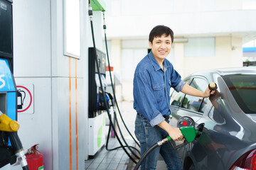 Happy cheerful Asian middle adult man refueling his car at self-service gas station, man refilling...