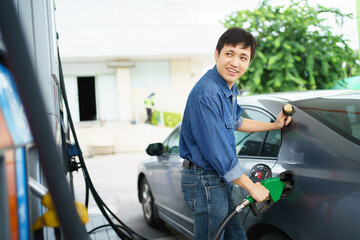 Happy cheerful Asian middle adult man refueling his car at self-service gas station, man refilling...